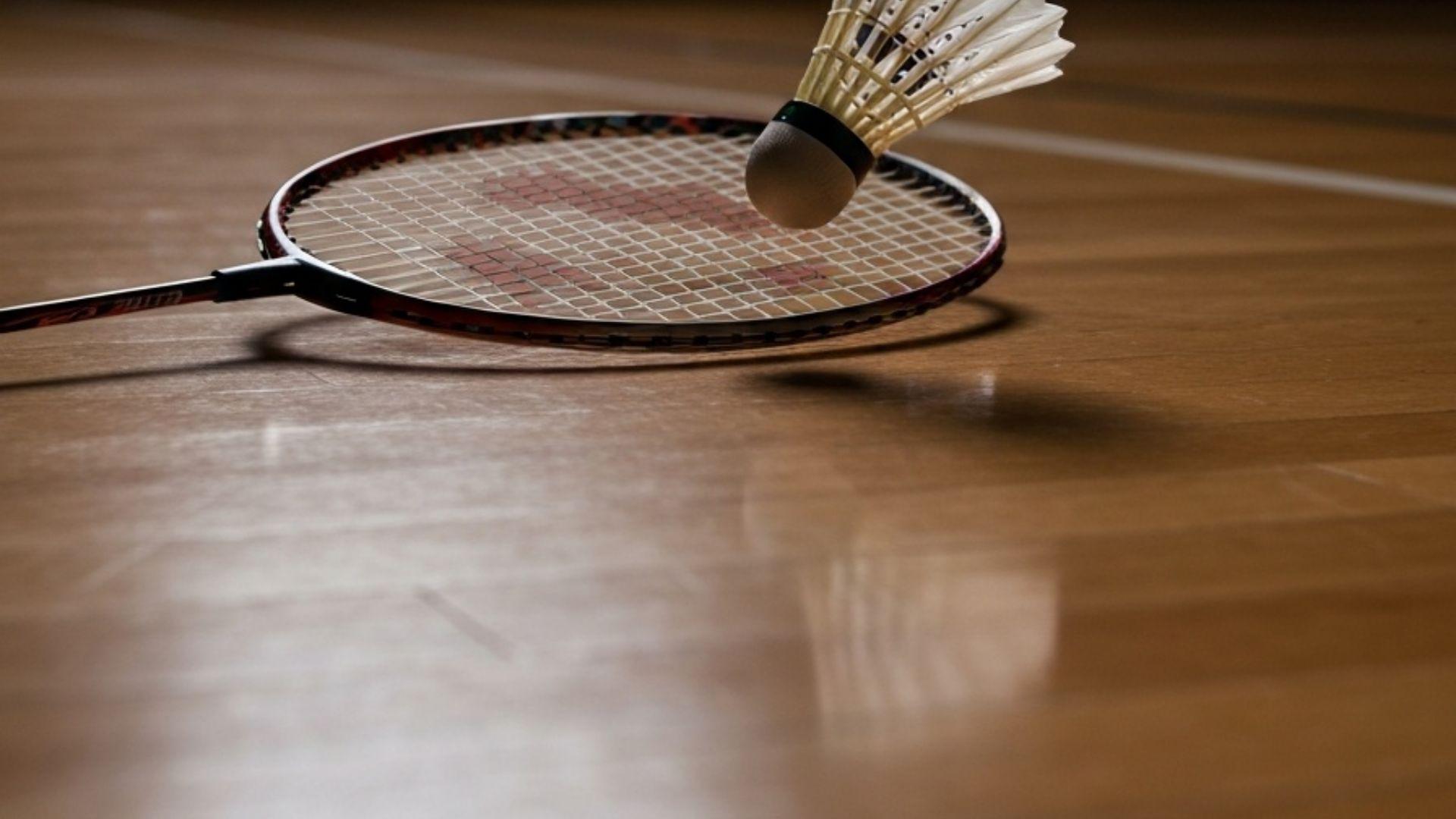 Badmintonracket med shuttle på inomhusplan med dramatisk sidobelysning
