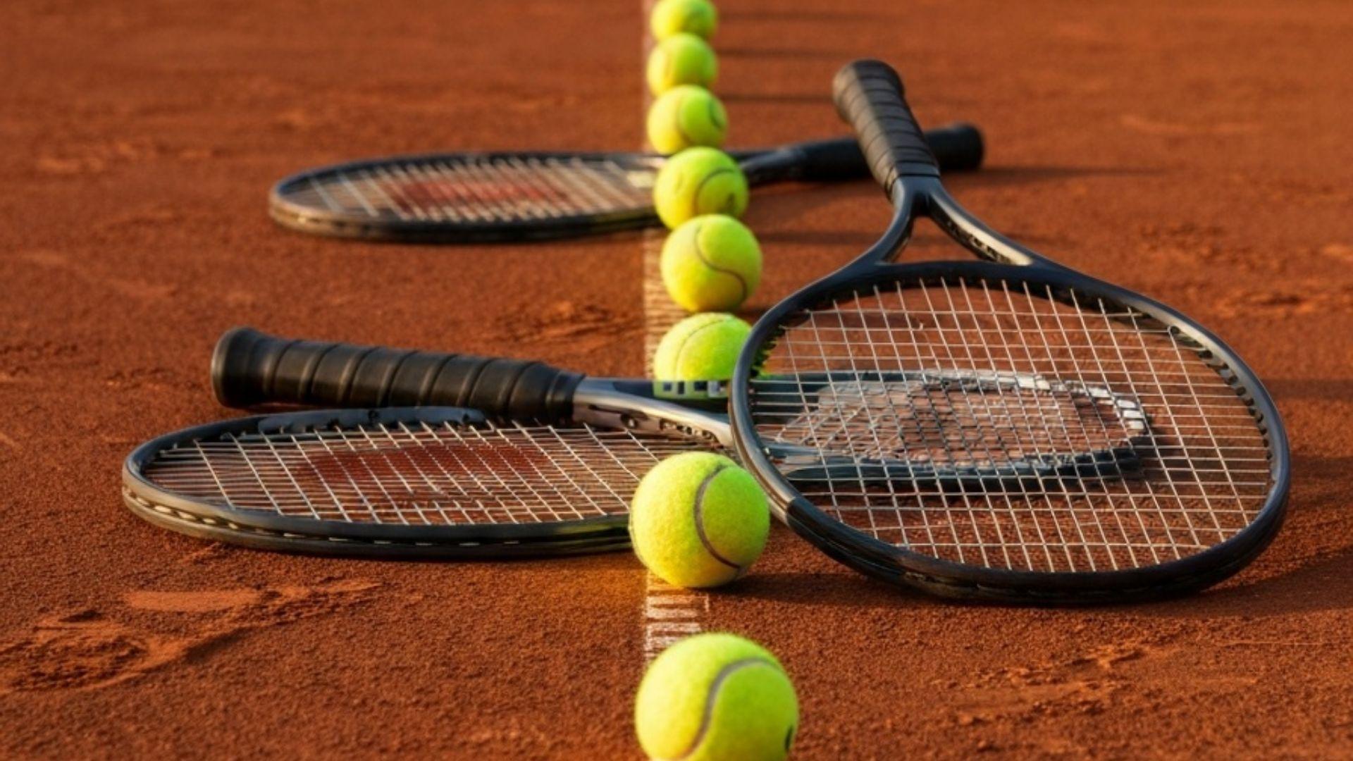 Tennisrack och bollar på grusbana i gyllene kvällsljus