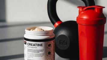 Öppen burk kreatinpulver med skopa bredvid kettlebell och shaker i modernt gym