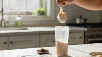 Proteinpulver skopas i shaker på marmorbänk i morgonljus