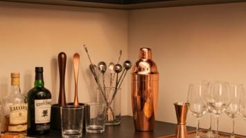 Stilren hemmabar med spritflaskor, kopparshaker och glas i varmt ljus