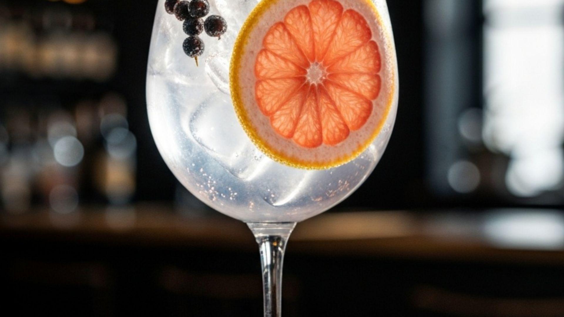 Perfekt garnerad gin & tonic i ballongglas med enbär och rosa grapefrukt, is som fångar ljuset mot mörk bardekör