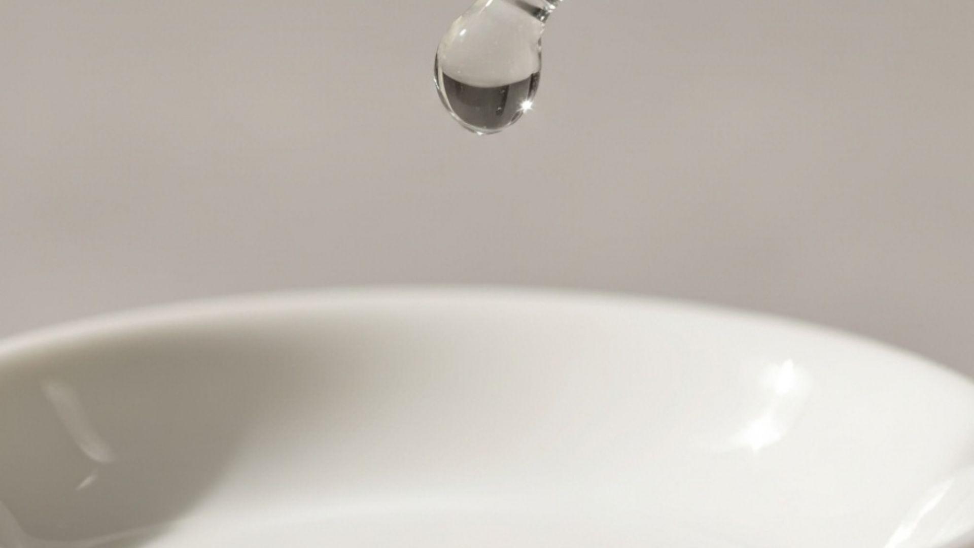 Närbild på en klar serumsdroppe på ett glasdropp ovanför en porslinsskål mot neutral bakgrund i beauty editorial-stil