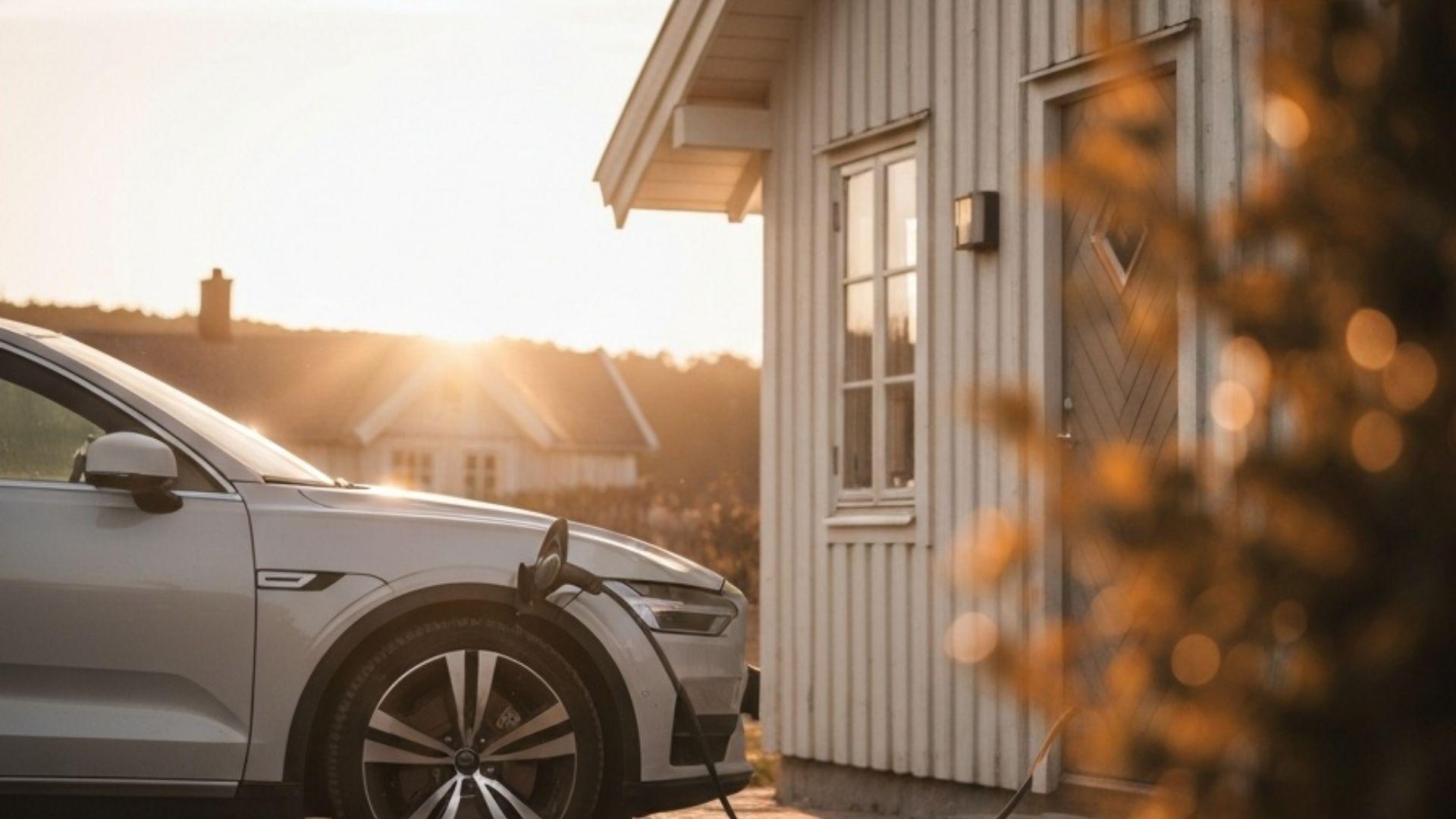 Modern elbil parkerad utanför ett skandinaviskt trähus med en typ 2-laddkabel inkopplad i seneftermiddagsljus